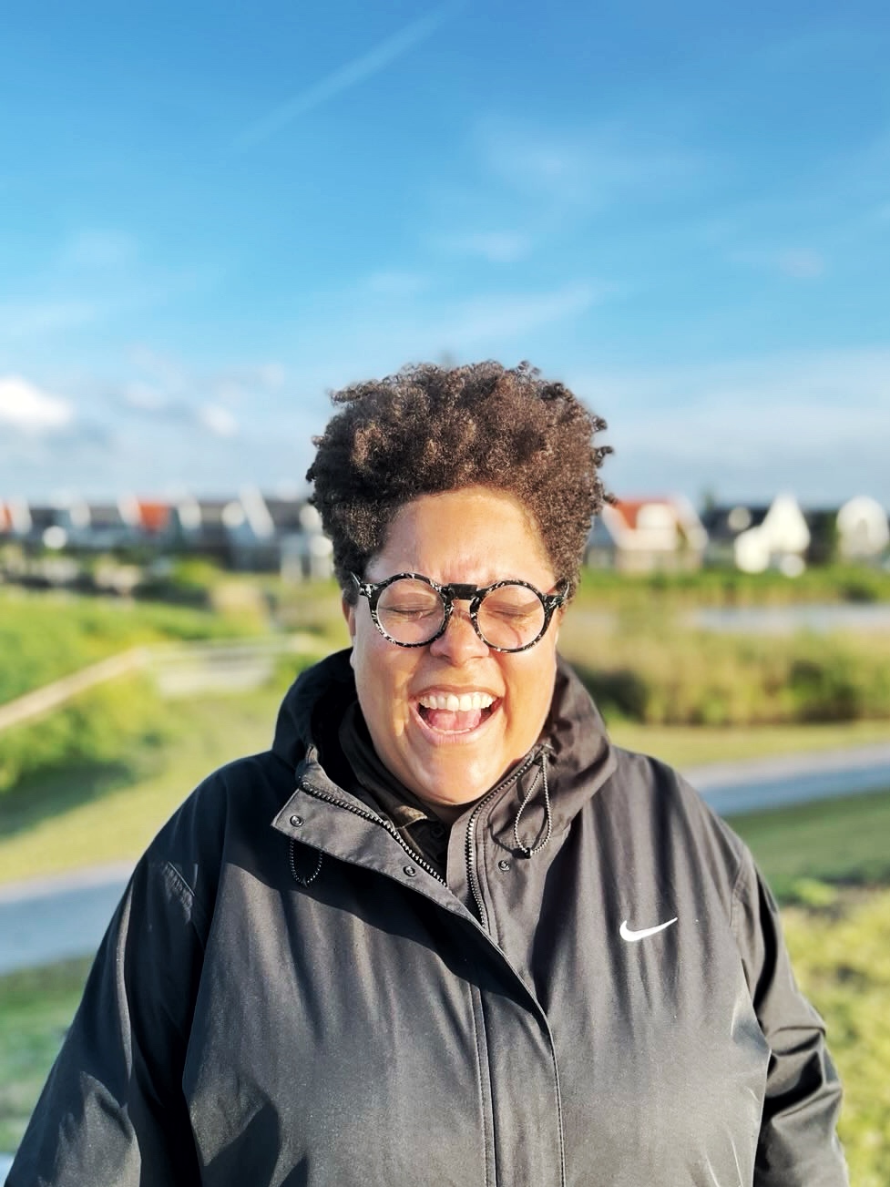 A person laughing with their eyes closed, Dutch landscape in the background